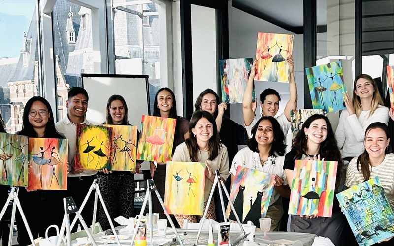 A company team holding up their paintings after a workshop in their office