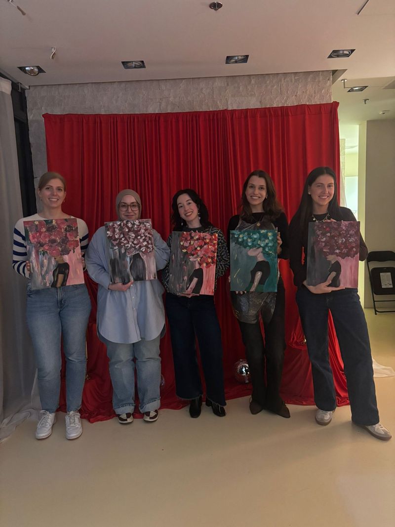Vijf vriendinnen met hun schilderijen voor het rode gordijn in de studio